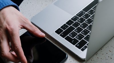 Person mit Handy am Laptop